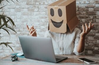 Happy modern online worker wearing smile carton box on head speaking in video call at the laptop